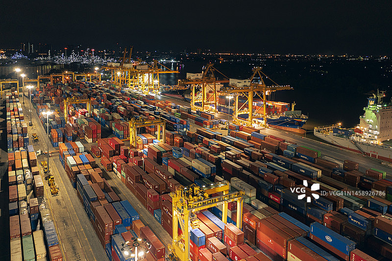 夜间卸货集装箱到集装箱货船的商业港口码头鸟瞰图，商业物流进出口运输。图片素材