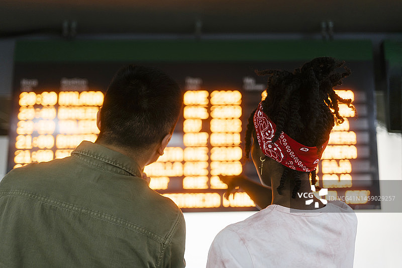 多种族朋友在火车站的出发指示牌上查看时间图片素材