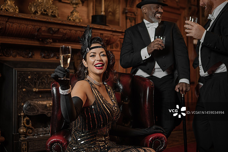在豪华棕色酒吧里的三位1920年代风格的英俊绅士和一位漂亮的黑发女子图片素材