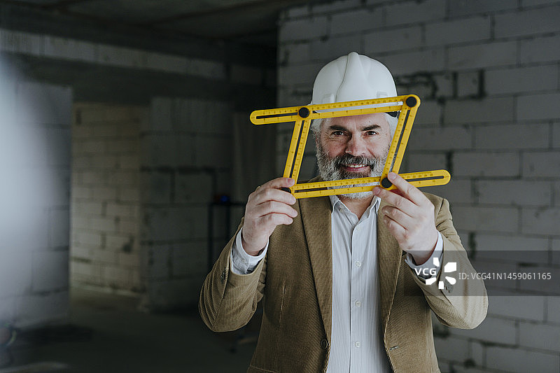微笑的建筑师戴着安全帽，用四折可调尺测量图片素材