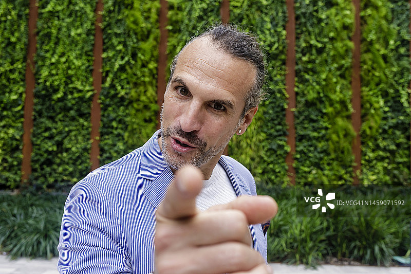 中年商人在树篱前用手指示意图片素材