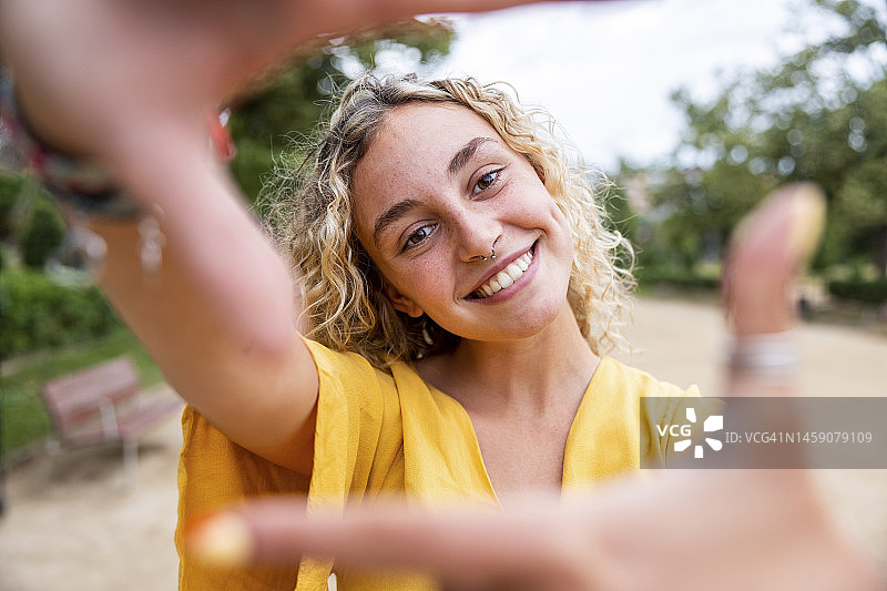 在公园里用手指做相框的快乐年轻女人图片素材