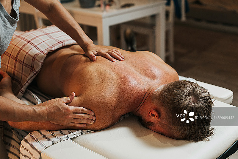 家庭按摩理疗。在厨房的家庭按摩。女人在家里给男人按摩。图片素材