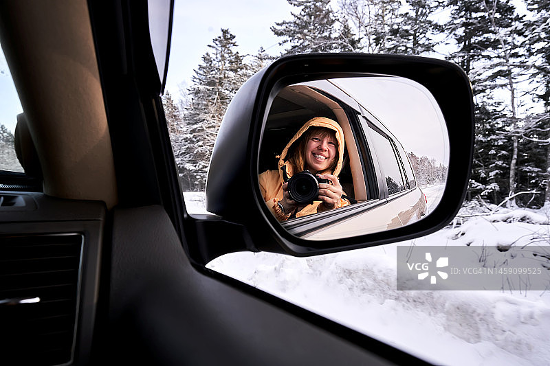 穿着黄色夹克的女人在汽车的后视镜里自拍图片素材