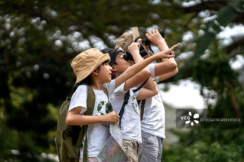 在自然考察中使用双筒望远镜观察树梢动物的儿童图片素材