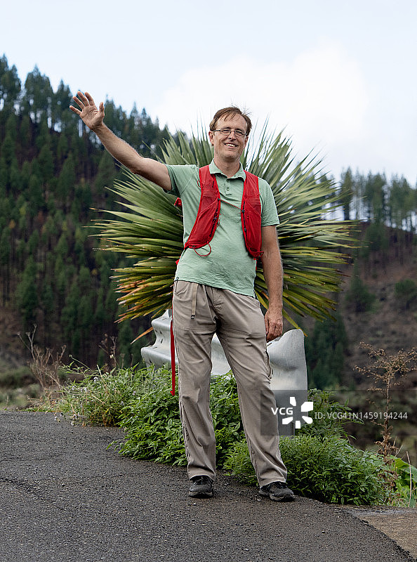 微笑的男徒步旅行者站在山路上挥手，西班牙加那利群岛大加那利岛图片素材