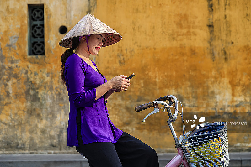 越南女子在会安古城骑自行车使用手机图片素材