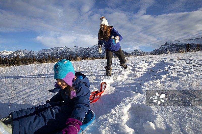 母亲推着小女儿从雪坡上滑下图片素材