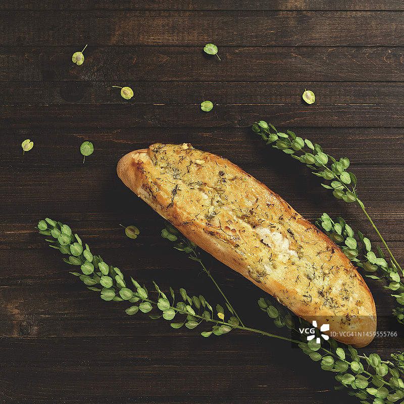 搭配奶酪、大蒜和香草的法棍。法国和地中海美食。木制背景上的新鲜糕点和绿色植物。俯视图。复制空间。深色背景图片素材