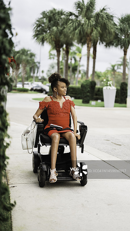 坐在轮椅上的快乐的年轻非裔美国残疾女性，身穿红裙，在美丽的户外肖像中图片素材