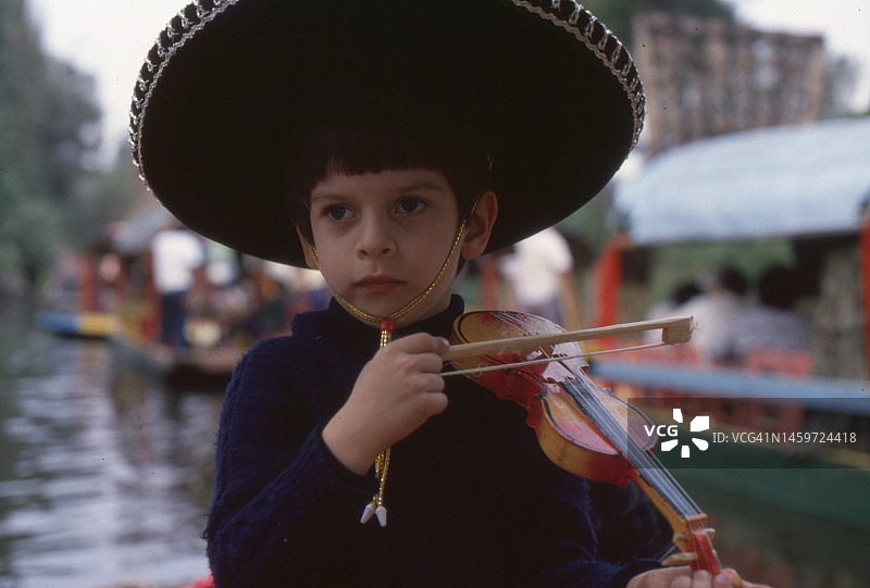 复古风墨西哥霍奇米尔科头戴查罗帽拉玩具小提琴的男孩照片，1979年图片素材