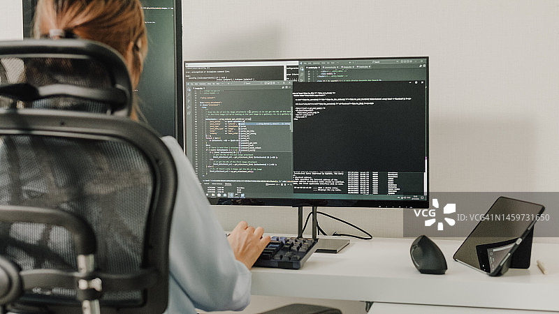 年轻亚洲女性软件开发人员使用电脑编写代码，坐在办公桌前，多个屏幕在家远程工作特写图片素材