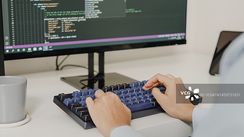 年轻亚洲女性软件开发人员使用电脑编写代码，坐在办公桌前，多个屏幕在家远程工作特写图片素材