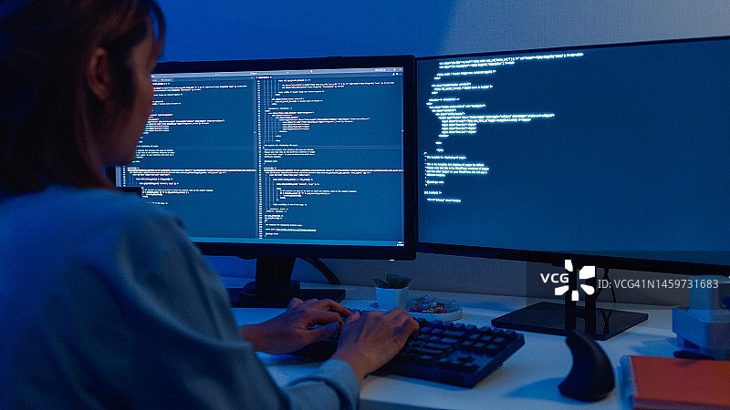 年轻的亚洲女软件开发人员使用电脑编写代码，坐在桌旁，多个屏幕，晚上在家远程工作图片素材