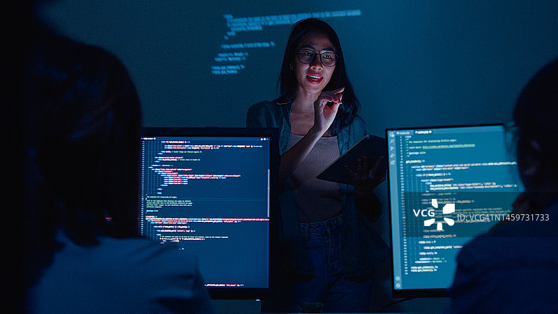年轻的亚洲女软件开发人员指导团队，与高管团队交谈，分析办公室夜间的源代码图片素材