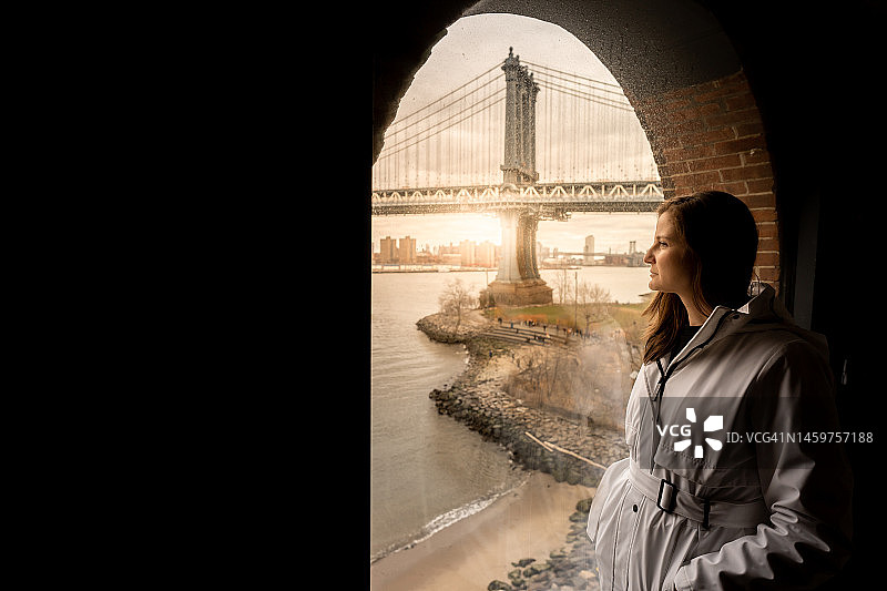 站在布鲁克林大桥附近的河边，手插在口袋里的女人图片素材