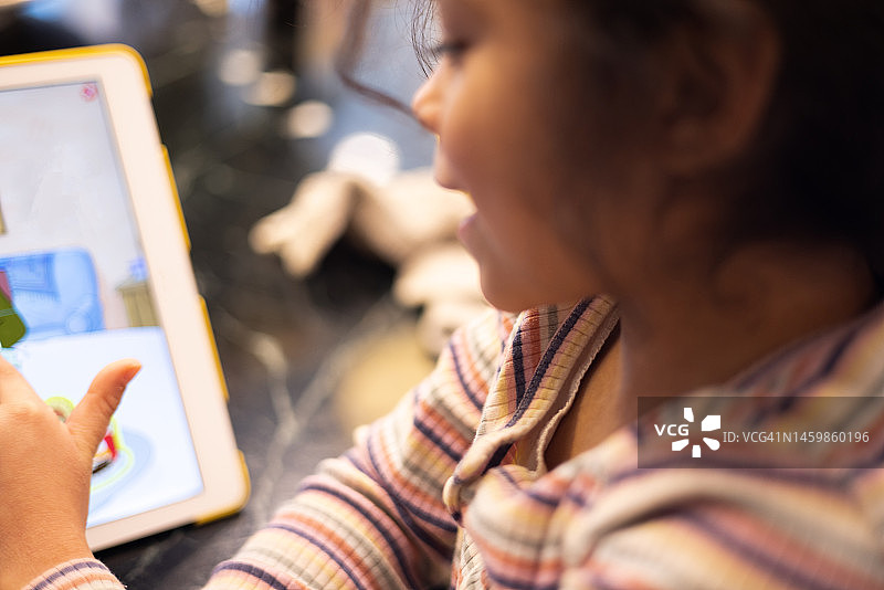 在厨房柜台上用平板电脑做作业或参加在线学习课程的年轻混血女孩图片素材