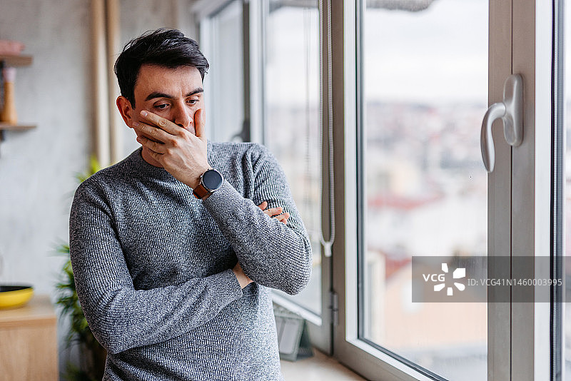 在家靠窗站着的悲伤青年男子图片素材