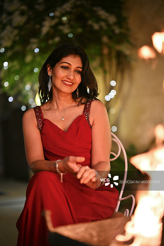 身穿红色派对礼服的美丽女人坐在篝火旁图片素材