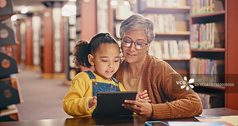 儿童，黑人家庭和平板电脑图书馆在线学习发展与教育和阅读。年长妇女教女孩孩子，同时流媒体网站，电子书和书籍一起学习知识图片素材