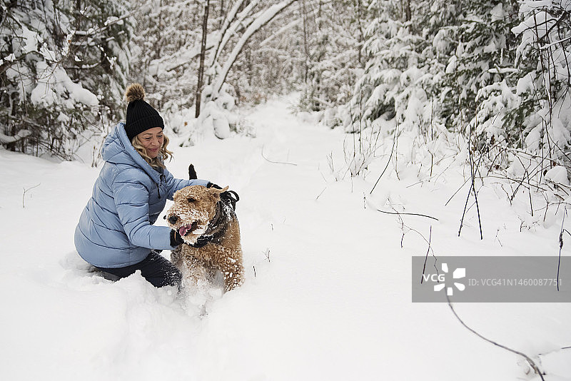在冬日雪地里迎接奔跑过来的狗的中年妇女图片素材