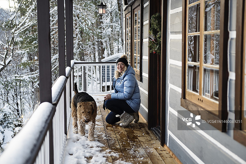 冬天，中年妇女和艾尔谷犬在小木屋阳台上图片素材