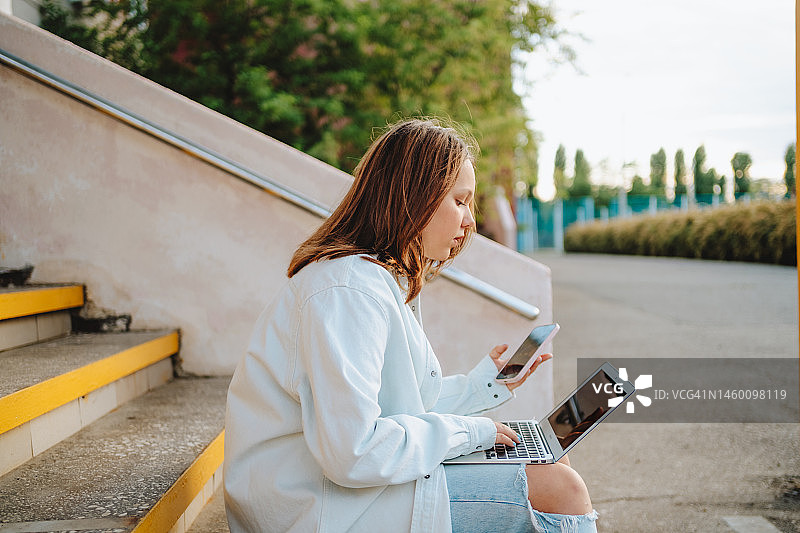 学校教育与远程作业：少女在后院楼梯上使用笔记本电脑和智能手机图片素材