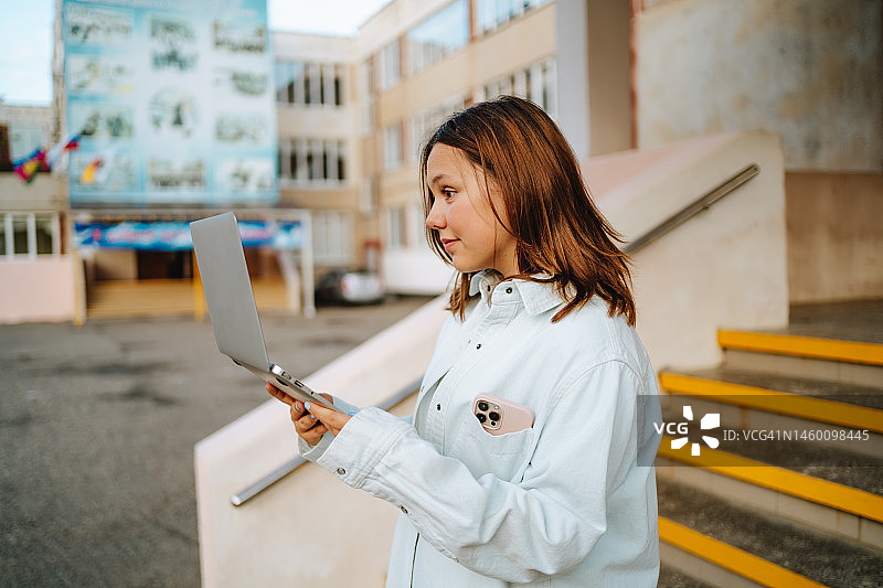 视频通话与青少年社交问题：在户外楼梯附近用笔记本电脑工作的女学生图片素材