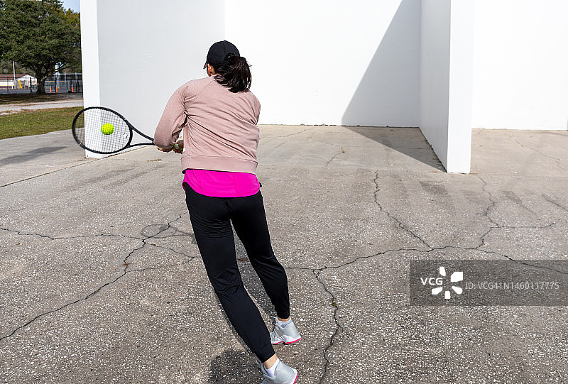 年轻女运动员在手球场墙壁上练习网球图片素材
