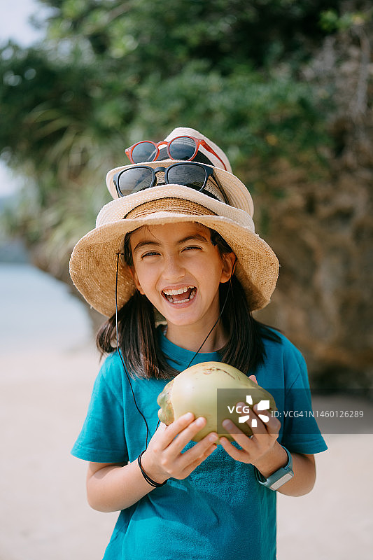 在海滩上戴着多顶草帽、拿着椰子和太阳镜的年轻女孩图片素材