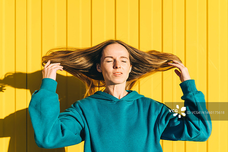 黄色背景下身穿蓝绿色卫衣的飘发女人图片素材