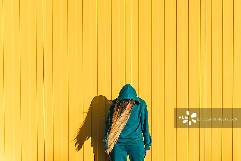 身穿蓝绿色运动衫的女人，黄色墙壁背景图片素材
