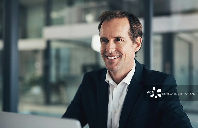 男商人，在办公室使用笔记本电脑，微笑，为企业想法、战略或项目计划而工作。快乐的男员工对着电脑微笑，期待好消息、日程安排或经济利润图片素材