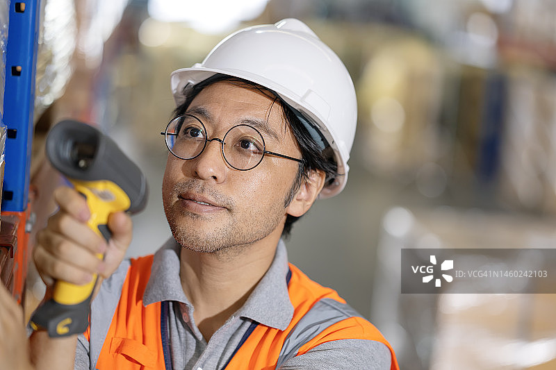 通过模块化移动技术改进仓库运营。一位日本仓库主管使用手持条形码阅读器扫描包裹上的产品代码，以确认库存盘点。图片素材