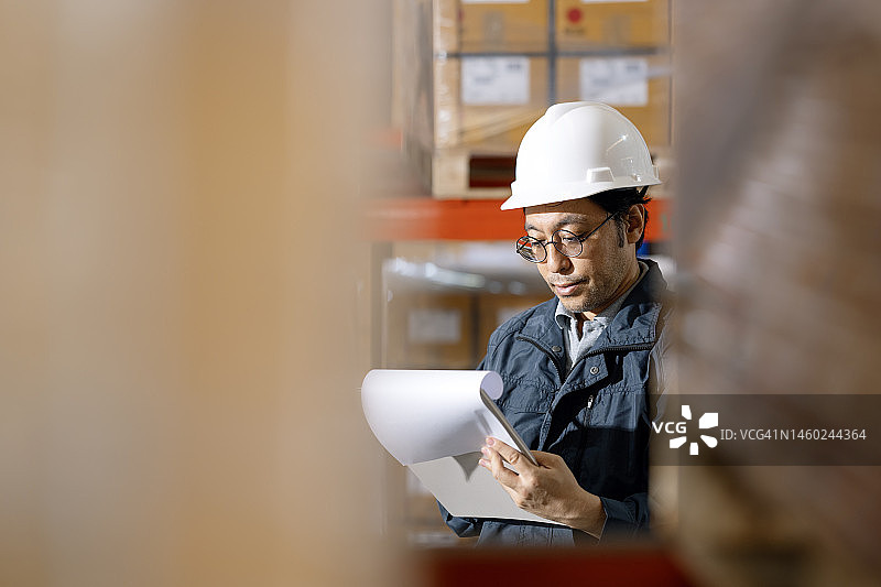 高质量的仓库运营始于人：一位日本仓库主管正在检查清单，审查配送仓库中的库存平衡图片素材