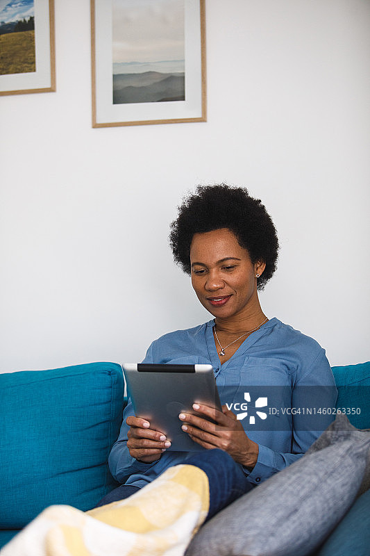 微笑的非洲裔女人在沙发上使用平板电脑图片素材