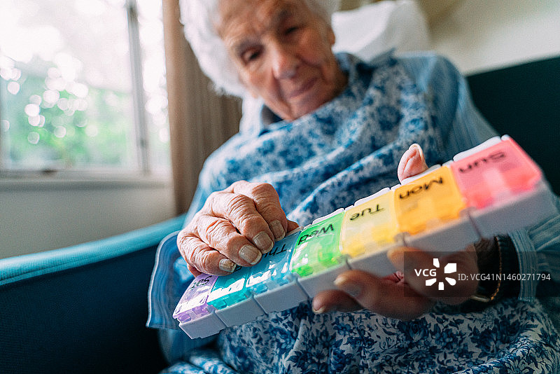 一位百岁老人仔细查看每周处方药和维生素补充剂整理盒图片素材