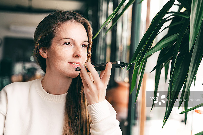 女商人或自由职业者在公共场所使用笔记本电脑和智能手机录制语音信息图片素材