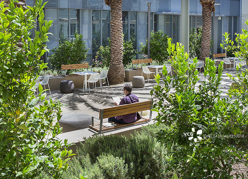 一位穿着便装的妇女坐在绿色节能建筑的花园庭院里。图片素材