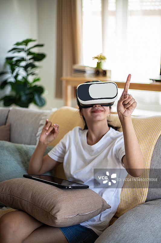 亚洲女士戴着虚拟现实耳机眼镜，在客厅的沙发上手势图片素材