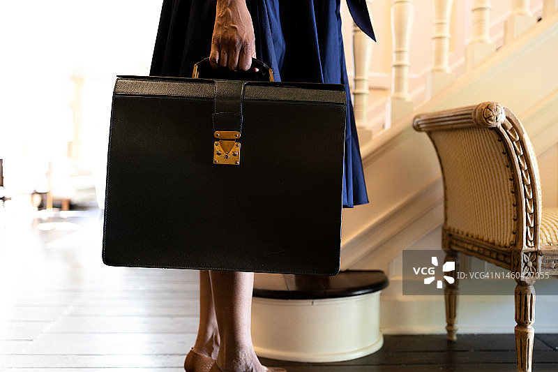 手提公文包、身穿喇叭裙和高跟鞋的黑人女性站在家中的门厅图片素材