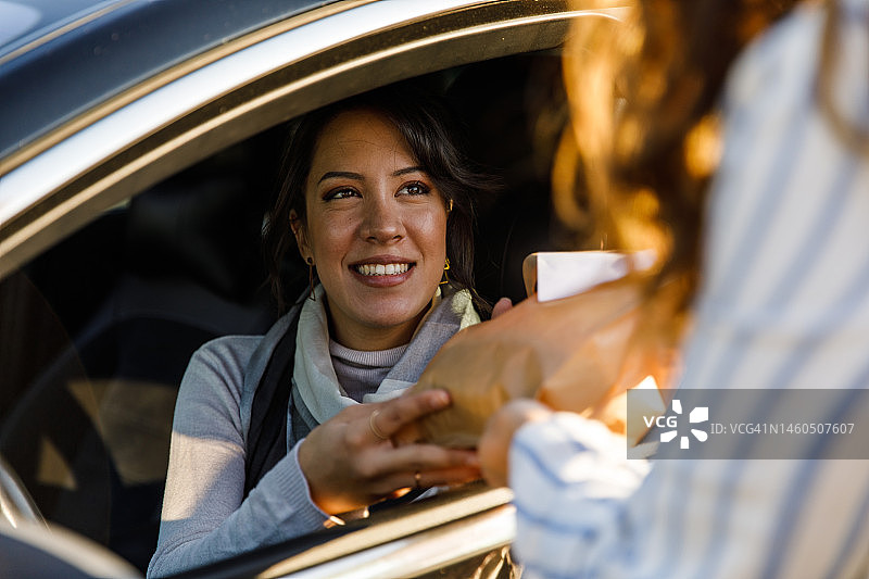 年轻女人坐在车里，从服务人员那里收到外卖订单图片素材