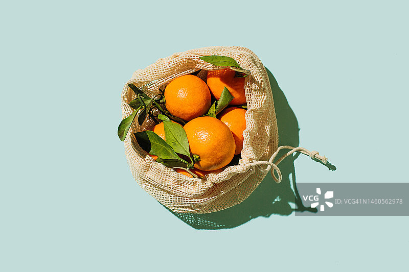 可重复使用的白色棉布袋中的新鲜橘子，蓝色背景，可持续的生活方式图片素材