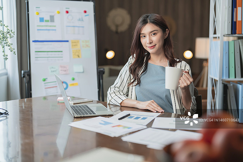 在客厅用笔记本电脑处理图表的亚洲微笑女性图片素材