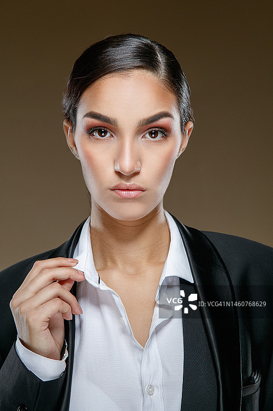 身穿黑色夹克、头发向后梳、看着镜头的漂亮年轻黑发女子肖像图片素材