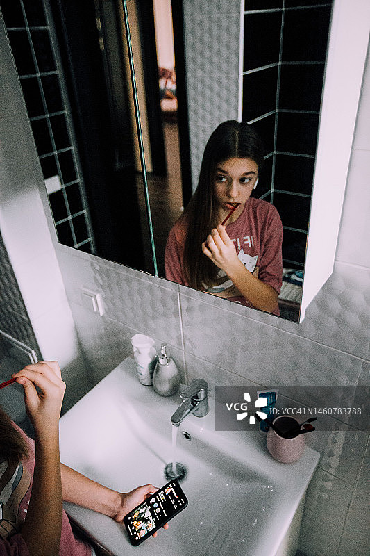 穿着睡衣、戴着耳机少女正在刷牙，看着镜子中的自己图片素材