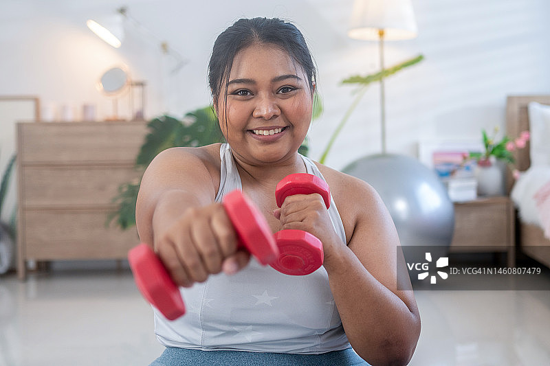 亚洲胖女人在卧室里尝试举重哑铃图片素材