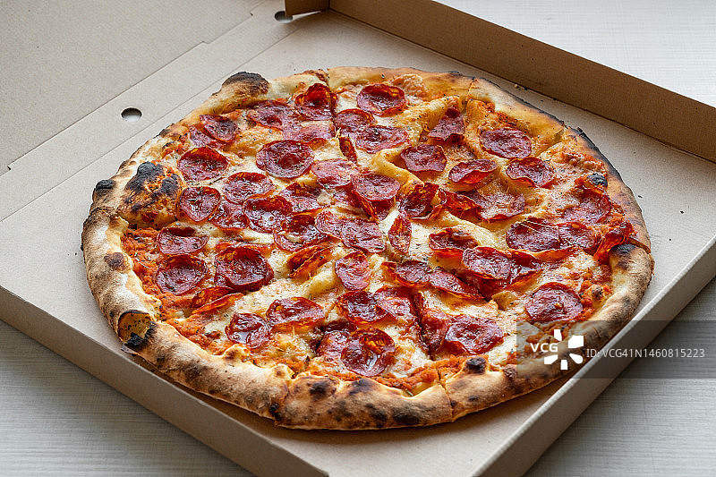 比萨店餐桌上的美味意大利比萨，配有比萨盒和外卖盒，切片比萨配有番茄、意大利辣香肠和奶酪，不健康的生活方式、暴饮暴食、垃圾食品、快餐概念，送货上门或工作场所图片素材