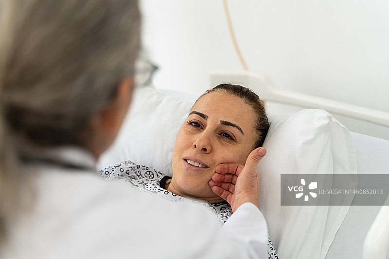 年长的医生在医院病床上探望并与女病人交谈图片素材