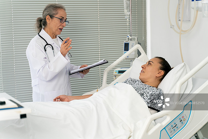 年长的医生在医院病床上探望并与女病人交谈图片素材